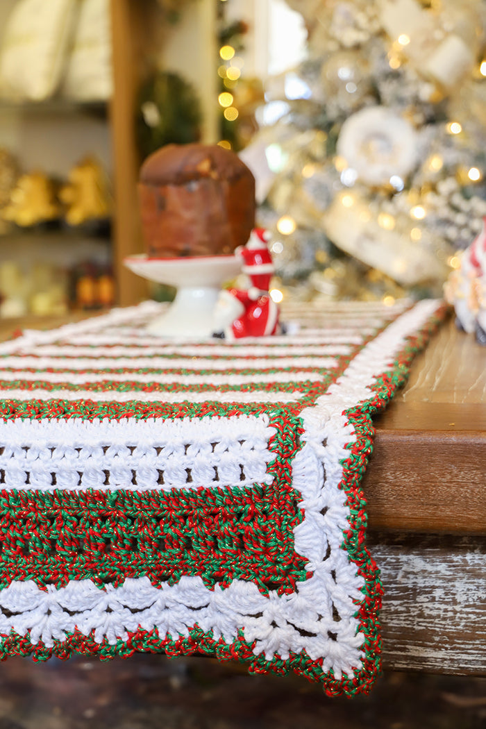 Círculo Barroco Maxcolor Sparkle – Cotton Yarn (216m / 200g) - A close-up of a handmade crocheted table runner with a white base, green and red textured stripes, and a decorative border, draped over a wooden table in a festive holiday setting.