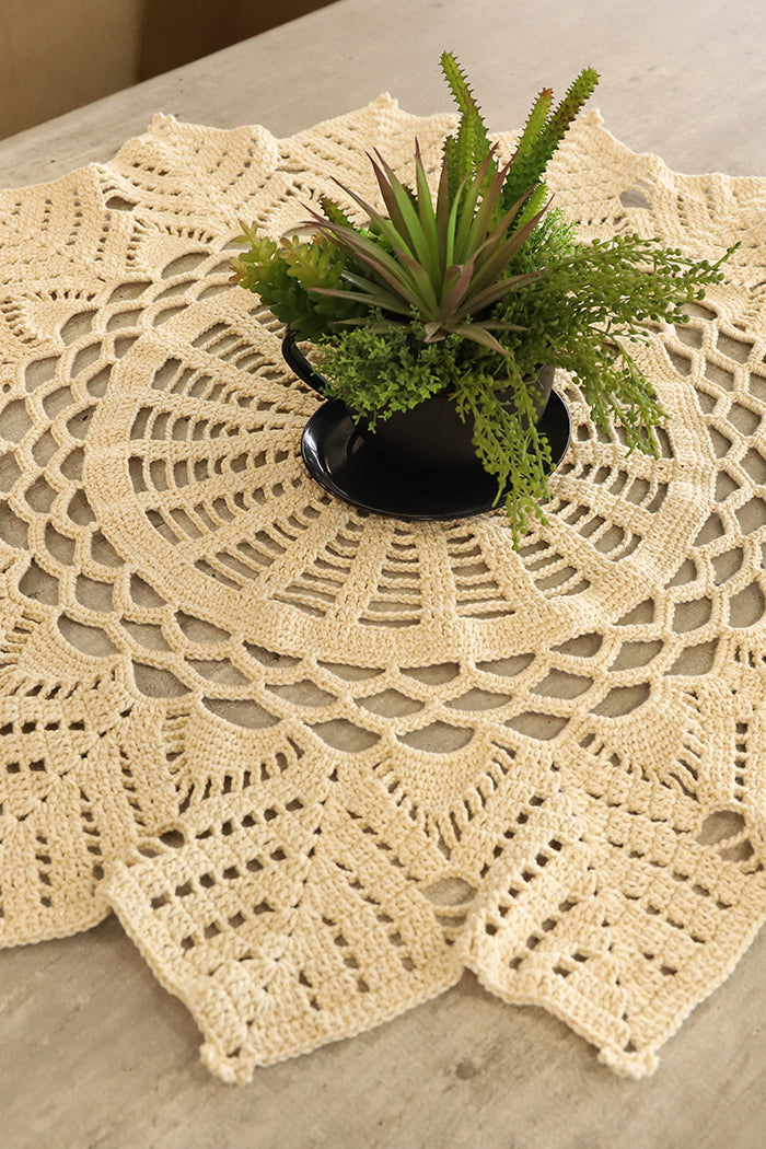 Circulo Barroco Natural Brilho - Natural Cotton Yarn Gold/Silver, 657m / 433m, 400g - A round cream-colored crocheted doily with an intricate lace pattern, styled on a light wood tabletop with a small potted succulent plant in the center.