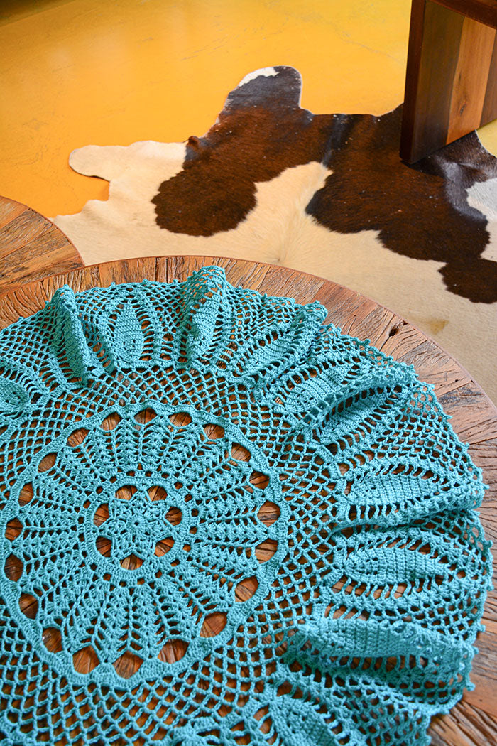 Circulo ANNE - 100% mercerized Cotton Yarn, 500m / 147g - Teal crocheted doily on a wooden surface with a cowhide rug in the background