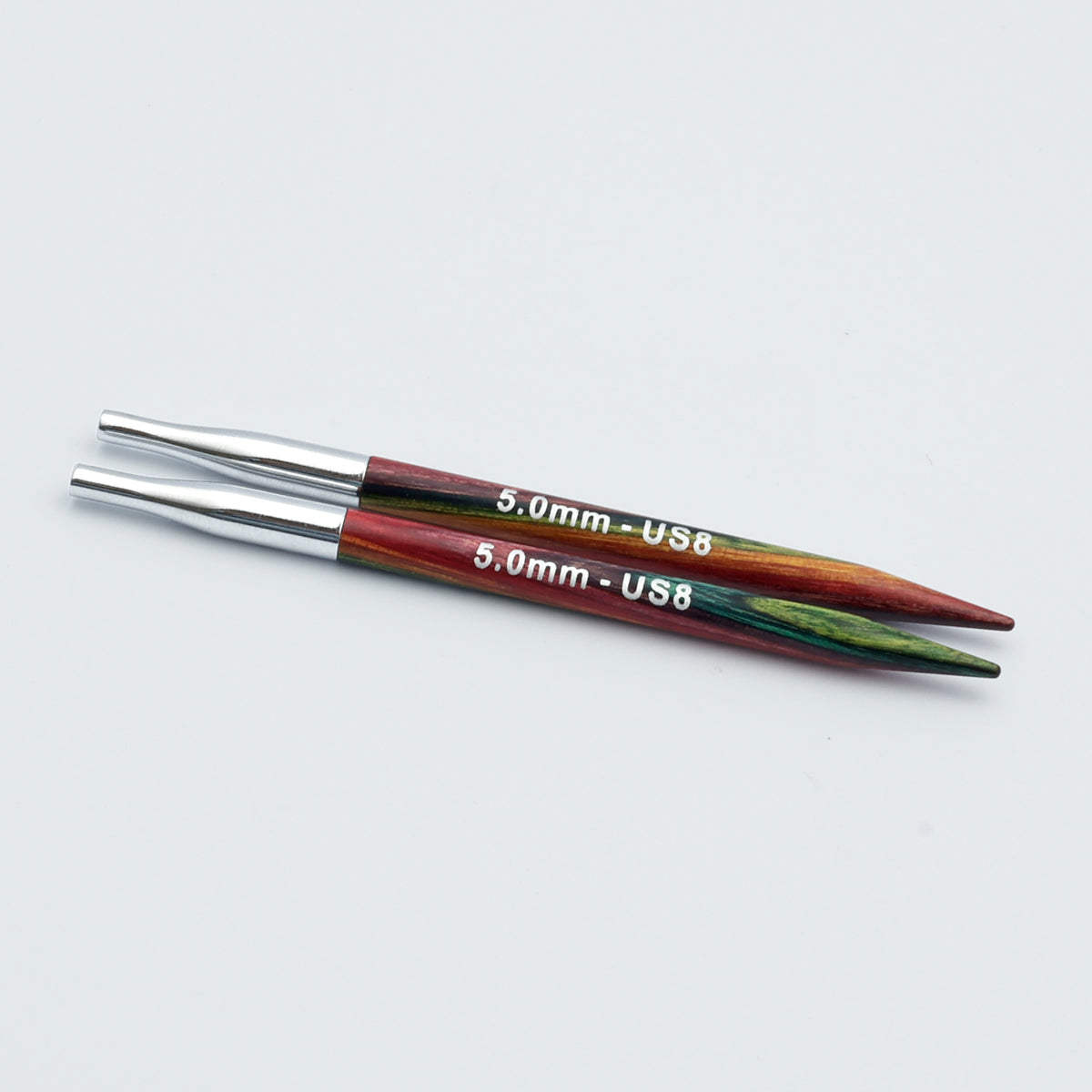 Knitpro-symfonie-2-interchangeable-needle-tips-special-10cm - Two 5.0mm US8 knitting needles with metallic silver tips and colorful wooden shafts showing red, green, and brown grain, on a light gray background.
