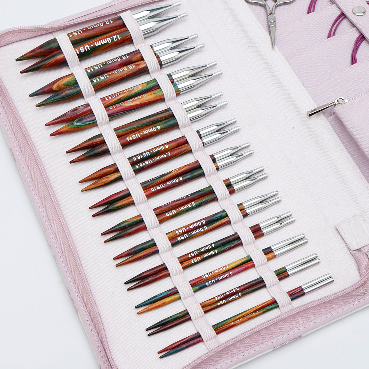 KnitPro Symfonie 2 Normal interchangeable needle set, 13 cm, Grande - A set of colorful knitting needles with silver metal tips, organized in a pink zippered case with white elastic loops. A pair of silver scissors is partially visible at the top right.
