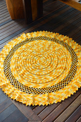 Circulo Barroco Multicolor Premium 4/6 - Brazilian Cotton Yarn, 226m/200g - A round yellow crocheted placemat with an intricate lace-like scalloped border, displayed on a dark brown wooden deck.