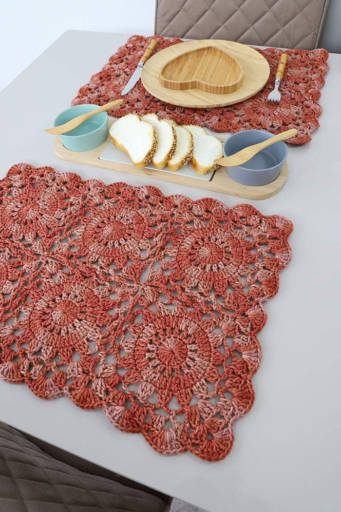 Circulo Barroco Multicolor Premium 4/6 - Brazilian Cotton Yarn, 226m/200g - A set of handmade crocheted table runners in a terracotta rust color, styled on a white dining table with a wooden heart-shaped plate, bowls, and sliced bread.