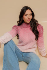 Círculo Marfim – Acrylic Gradient Cake Yarn (400 m / 200 g) - A woman wearing a fuzzy pink mock-neck sweater with contrasting light pink and white sleeve cuffs, paired with light blue jeans, seated against a solid beige background.