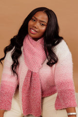 Círculo Marfim – Acrylic Gradient Cake Yarn (400 m / 200 g) - A woman wearing a fuzzy knit two-tone pink and white striped sweater with a matching knit scarf, posed against a solid warm tan background.