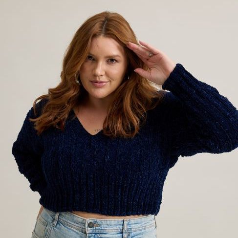 Círculo Velvet – 100% Polyester Chenille Yarn (165 m / 100 g) - A woman with wavy light brown hair wearing a dark navy blue ribbed knit cropped sweater and light wash blue jeans, posing against a solid light beige background.