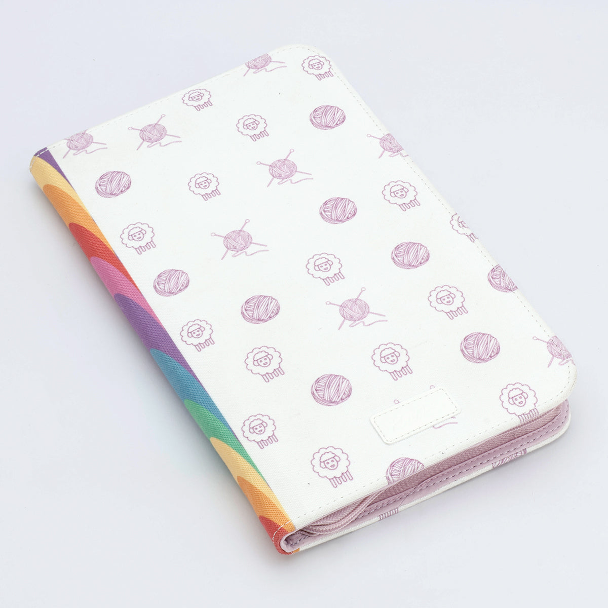 KnitPro Symfonie 2 Normal interchangeable needle set, 13 cm, Grande - A white folio-style tablet case with a repeating pattern of pink yarn balls and sheep, featuring a colorful rainbow stripe along the left edge and a light pink zipper.